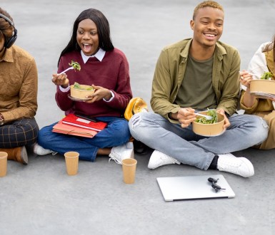 Students sit on the ground eating salad with their text books