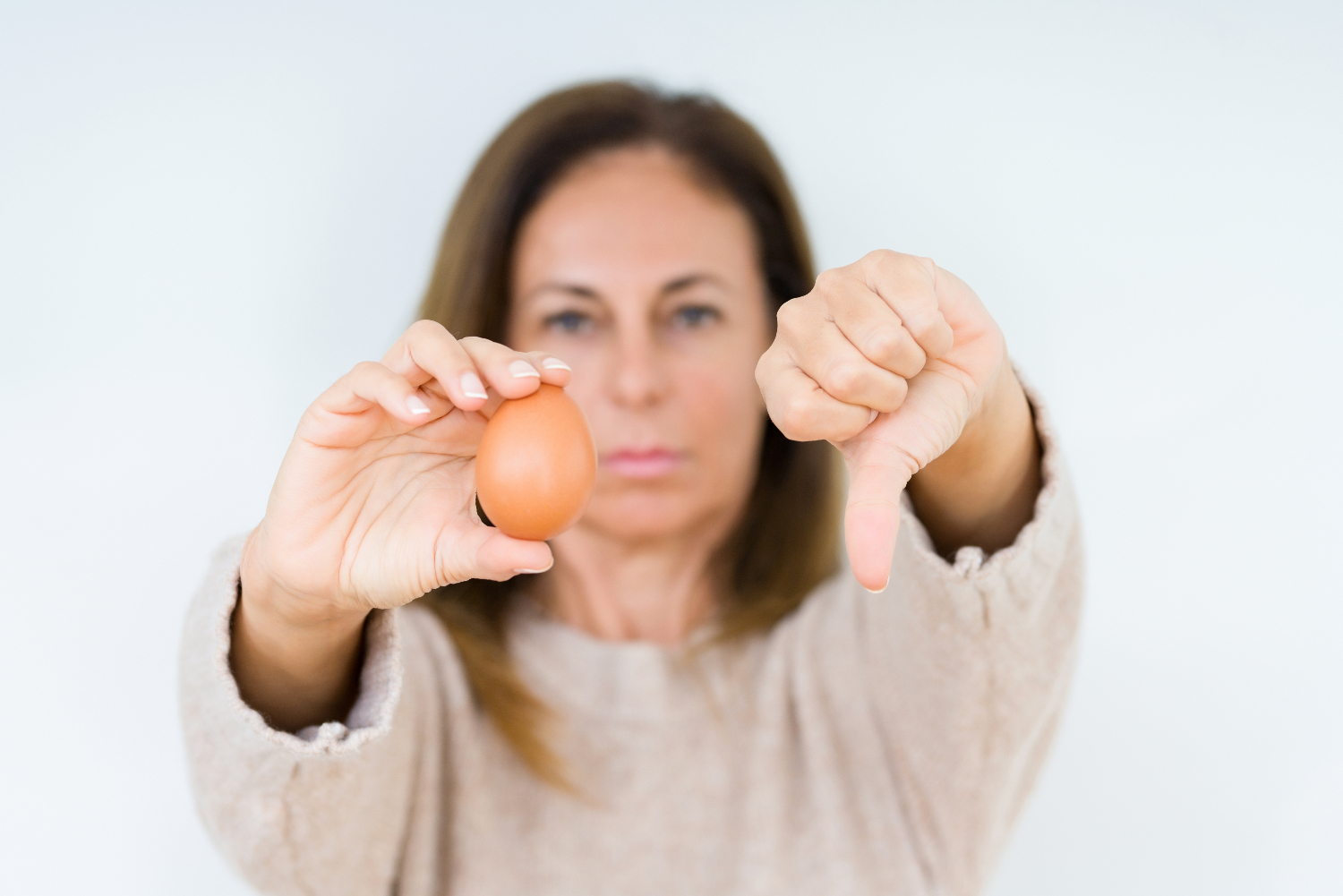 A woman holds an egg with a thumb down