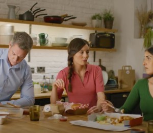 screenshot of tv advert in which two women and one man are sat down eating a meal