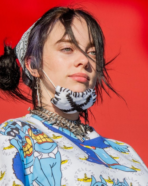 Billie Eilish on stage with a mask on her chin.